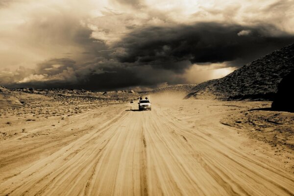 El coche se mueve a través del desierto sobre la arena en medio de la puesta de sol