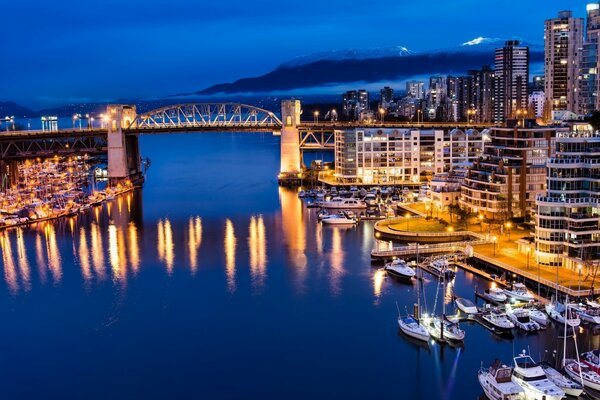 Puente sobre el río que conecta partes de la ciudad de la noche en las luces en el fondo de la montaña en la niebla blanca