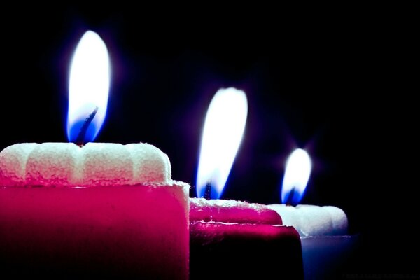 La llama de las velas multicolores sobre el fondo oscuro
